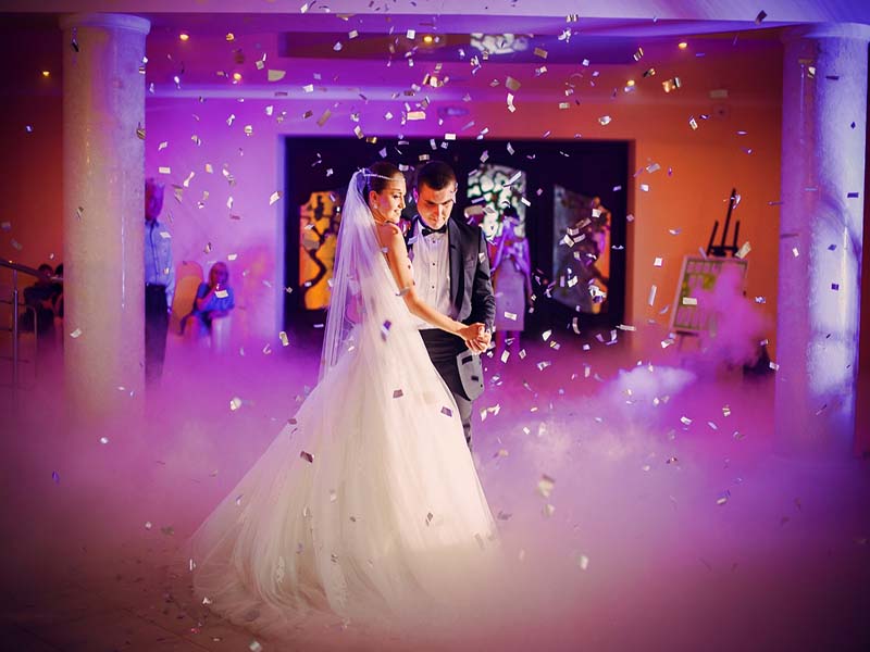 Couple dancing in a purple-lit ballroom with white and gold confetti falling from the ceiling.