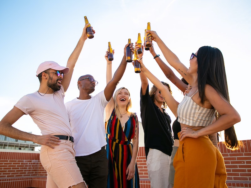 Group of friends celebrating on a rooftop with beer bottles in summer.